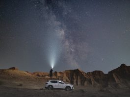 picture of a person standing on the car in the dessert looking to the stars with a flashlights