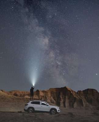 picture of a person standing on the car in the dessert looking to the stars with a flashlights