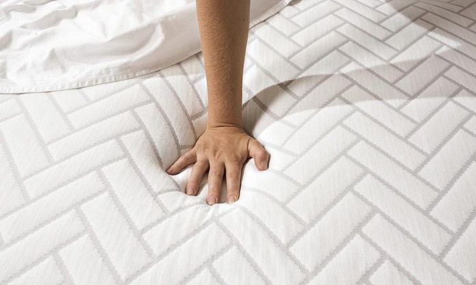 hand pushing down on soft mattress